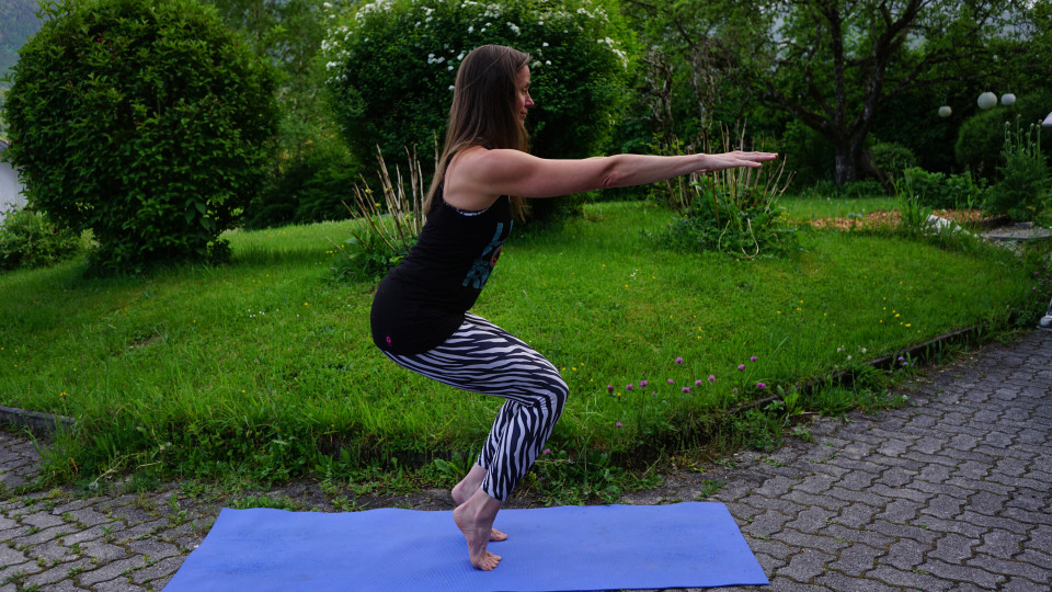 mit der Ausatmung wieder abstellen oder kraftvoller für die Beine mit dem Ausatmen in einer Hocke kommen (Utkatasana) mit den Armen parallel zum Boden (wahlweise die Fersen abstellen oder in der Hocke auf den Zehen balancieren)